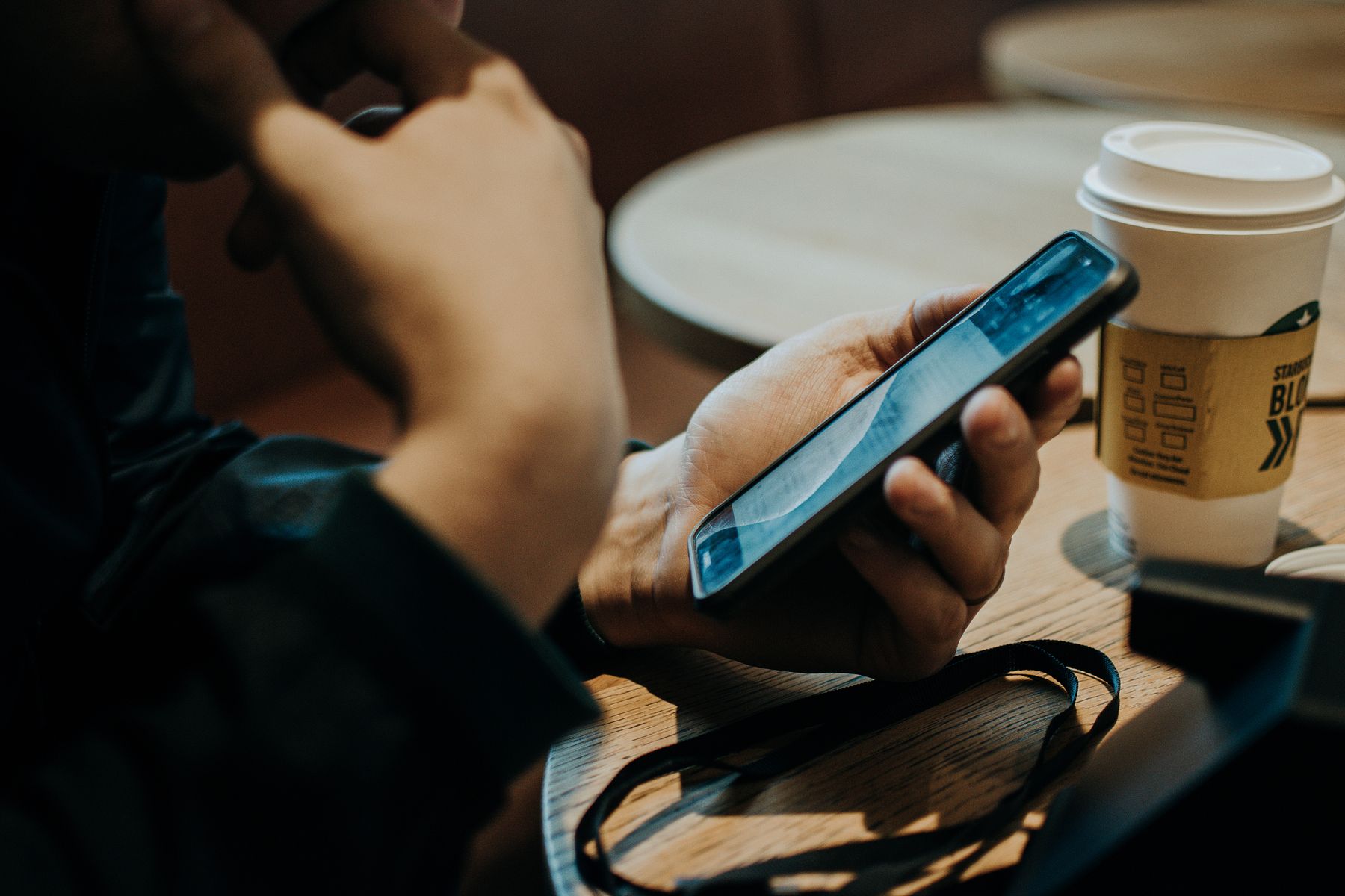 Hand met smartphone en koffie op een cafe tafel
